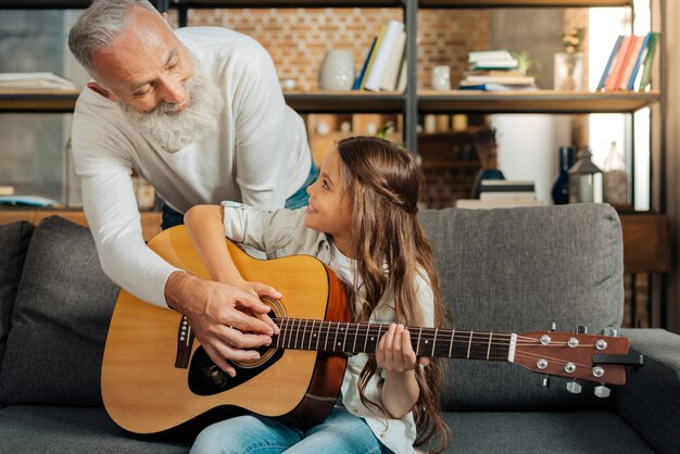 Sentiero per sognare. Adorabile bambina che impara a suonare una chitarra mentre il suo amato nonno la mostra a strimpellare accordi sulla chitarra