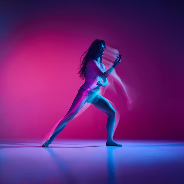 Sentimenti giovane donna che balla stile di danza moderna su sfondo di studio rosa gradiente in neon con