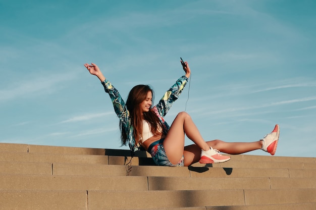 Sentirsi liberi e felici. Attraente giovane donna in abbigliamento sportivo che sorride mentre è seduta sui gradini all'aperto