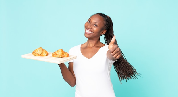 Sentirsi orgogliosi, sorridere positivamente con il pollice in alto e tenere in mano un vassoio di croissant