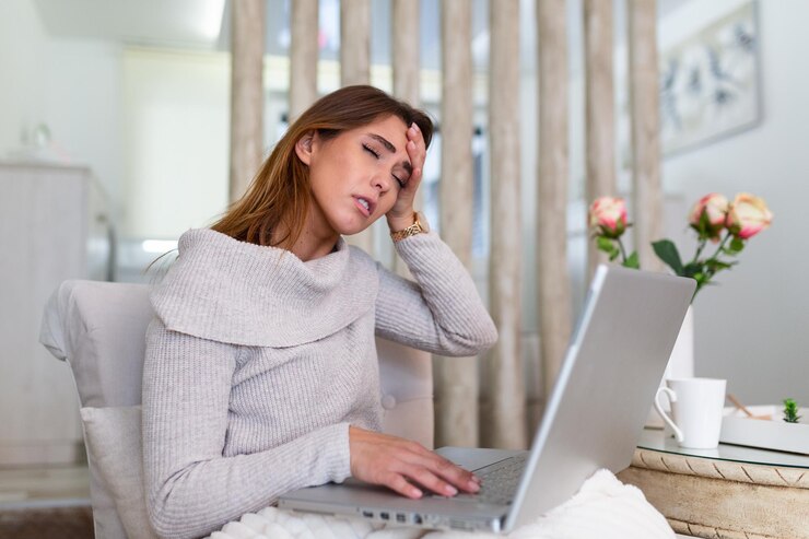 Foto sentirsi stremato. giovane donna frustrata che sembra esausta mentre è seduta al suo posto di lavoro a casa. libero professionista oberato di lavoro con mal di testa