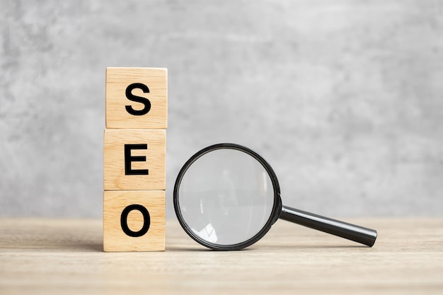 SEO (Search Engine Optimization) testo blocchi di legno cubo e mano che tiene la lente d'ingrandimento sul tavolo. Idea, strategia, pubblicità, marketing, parola chiave e concetto di contenuto