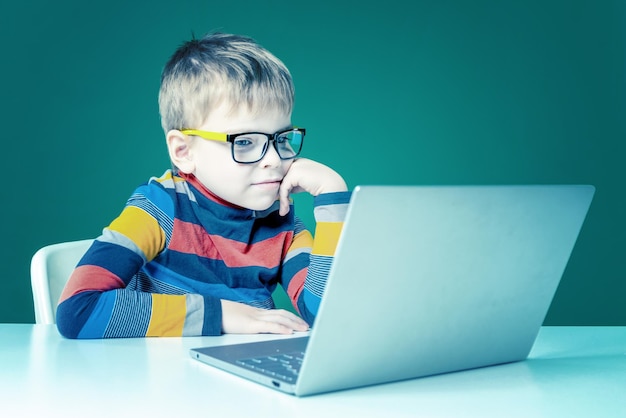Seorang anak laki-laki berkacamata sedang duduk dengan laptop, close-up