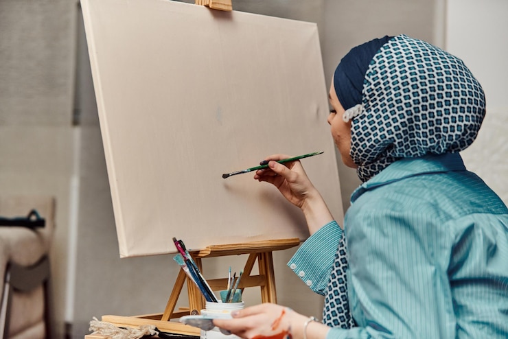 Seorang wanita berhijab melukis di atas kanvas dengan kuas dan tempera