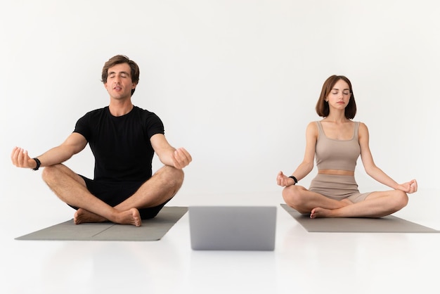 Serio calmo giovane europeo e signora in abbigliamento sportivo che pratica yoga con il computer portatile