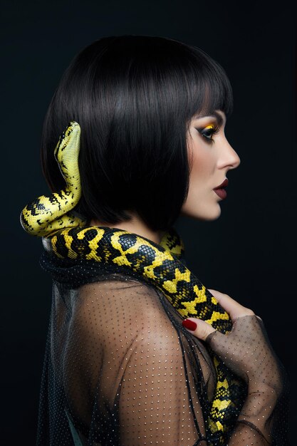 Serpente giallo pitone taglio di capelli corto donna di bellezza sul collo. Un serpente giallo sulle spalle di una ragazza. Trucco ombretto giallo di bellezza, rossetto bordeaux scuro