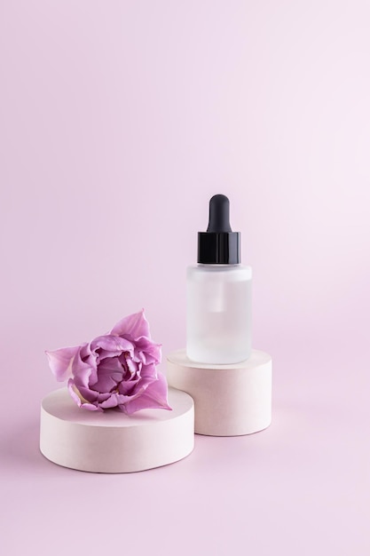 Serum per prodotti di bellezza di moda in bottiglia cosmetica di vetro con gocciolino per la cura della pelle del viso e del corpo in piedi su un podio rotondo di cemento con un fiore di tulipano