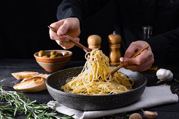 Serve pasta tradizionale italiana da una padella. Mani maschii che prendono gli spaghetti in cucchiaio e forchetta, colpo in scuro