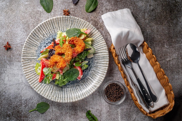 Serve un piatto dal menu del ristorante. Gamberi reali in pastella con limone e insalata su un piatto contro un tavolo di pietra grigia, un gustoso antipasto