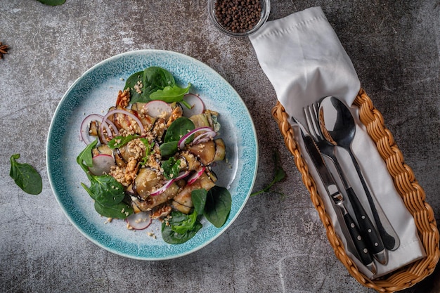 Serve un piatto dal menu di un ristorante. Melanzane ripiene con cipolle, spinaci verdi e noci su un piatto sullo sfondo di un tavolo di pietra grigia