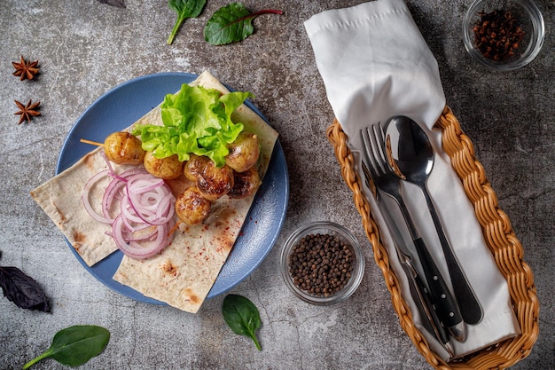 Serve un piatto dal menu di un ristorante. Patate al forno in stile country alla griglia con pane pita, erbe aromatiche e cipolle su un piatto blu sullo sfondo di un tavolo di pietra grigia