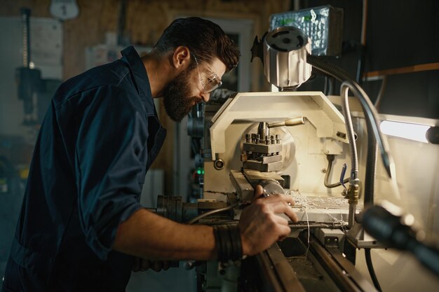 Servicista che gira il tornio per regolare i pezzi di ricambio Lavoro di riparazione in officina