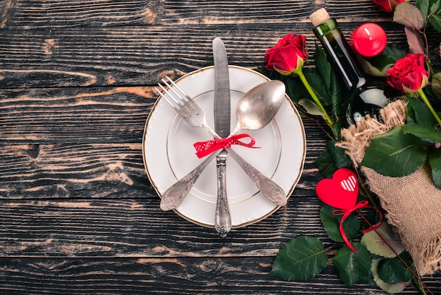 Servire la tavola per festeggiare San Valentino. Posate, piatto, rose. Su uno sfondo di legno. Vista dall'alto. Spazio libero per il tuo testo.