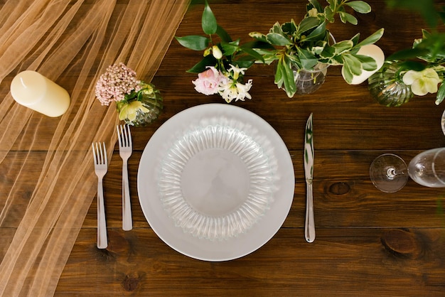 Servire una tavola festiva. Bellissimi piatti e posate, fiori in vasi su un tavolo di legno. Vista dall'alto