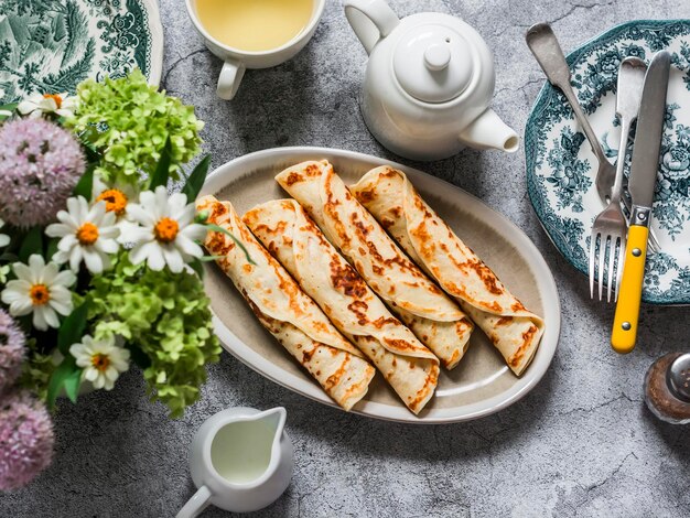 Servito colazione brunch crepes da tavola ripiene di tonno avocado e uova piatti vintage un bouquet di fiori estivi su sfondo grigio vista dall'alto