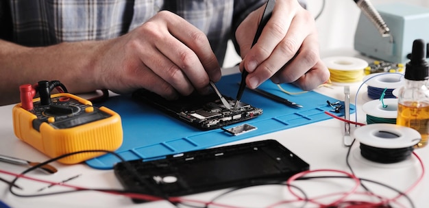 Serviziere che controlla lo smartphone rotto per la riparazione in un laboratorio di riparazione