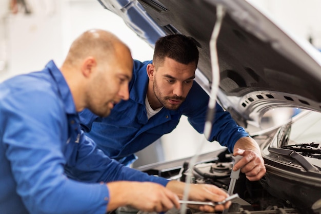 servizio auto, riparazione, manutenzione e concetto di persone - meccanici con chiave inglese che riparano auto in officina