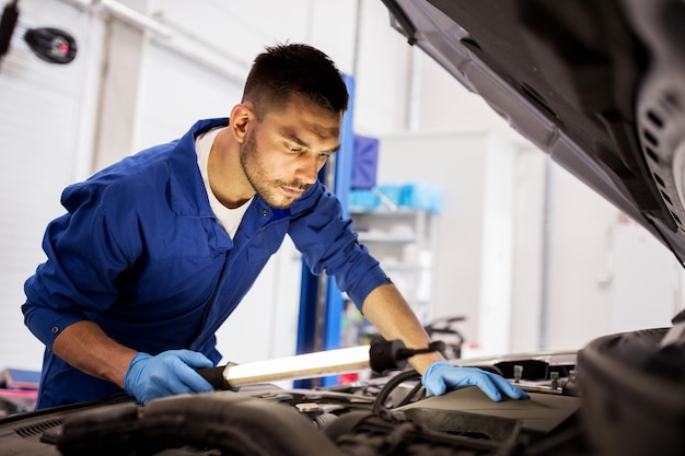 servizio auto, riparazione, manutenzione e concetto di persone - meccanico automobilistico con lampada che lavora in officina