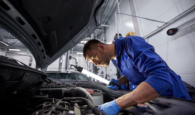 servizio auto, riparazione, manutenzione e concetto di persone - meccanico automobilistico con lampada che lavora in officina