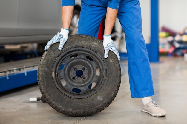 servizio auto, riparazione, manutenzione e concetto di persone - uomo meccanico con pneumatico ruota in officina