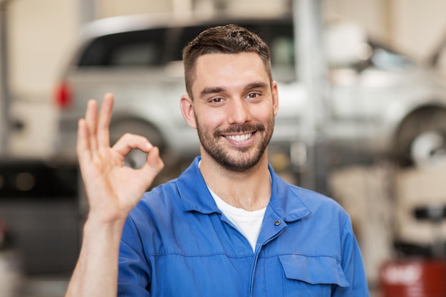 servizio auto, riparazione, manutenzione e concetto di persone - uomo meccanico o fabbro sorridente felice che mostra il segno della mano ok in officina