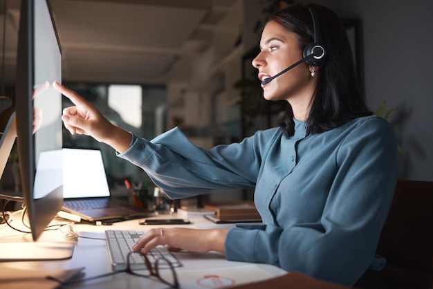 Servizio clienti del call center e donna di notte che lavora in ufficio indicando lo schermo del computer e aiutando il cliente Telemarketing dell'assistenza clienti e consulente femminile che parla parlando e online