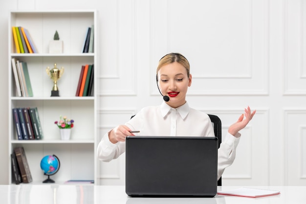 Servizio clienti donna carina in camicia bianca con auricolare e computer che parla e sorride