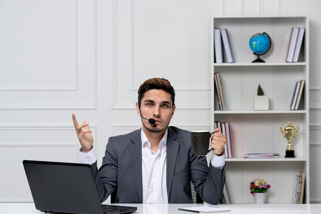 Servizio clienti grazioso gentiluomo con computer in abito da ufficio grigio con tazza di caffè