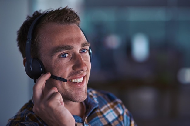 Servizio con un sorriso Inquadratura di un felice agente del servizio clienti che indossa un auricolare mentre è seduto in ufficio
