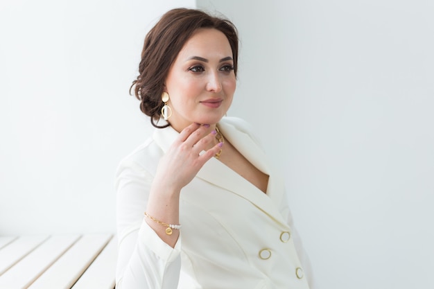 Servizio di alta moda di giovane donna bruna con acconciatura elegante in abito bianco al chiuso. Attività commerciale