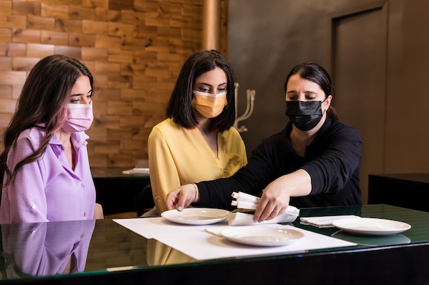 Servizio di cameriera con maschera facciale e distanza sociale per un cliente di donne ispaniche Personale professionale del ristorante di sushi nella nuova vita normale con la pandemia di covid19 Colore giallo 2021 anno
