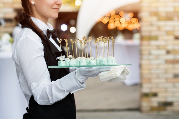 Servizio di catering. Cameriere con un vassoio di antipasti. Festa all'aperto con finger food, dolci.