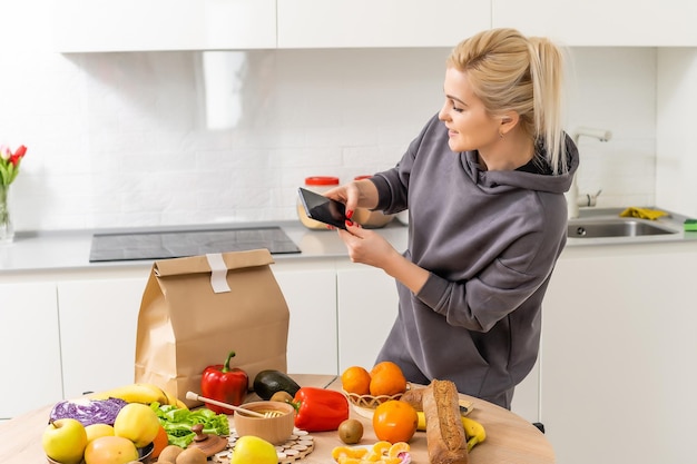 Servizio di consegna cibo - donna che tiene smartphone davanti alla scatola della spesa.