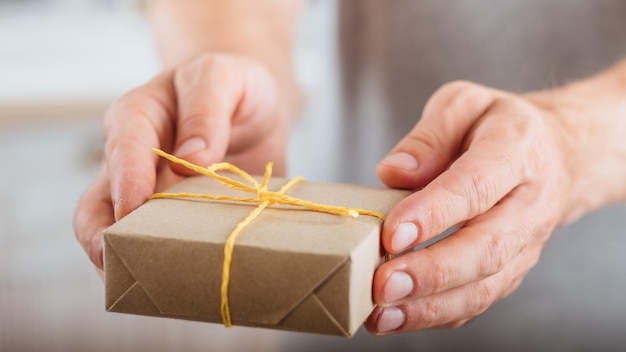 Servizio di consegna in un giorno speciale Primo piano di una confezione regalo con involucro di carta fatta a mano nelle mani dell'uomo