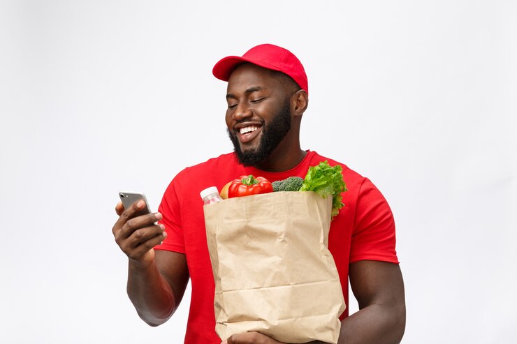 Foto servizio di consegna - ritratto di uomo di consegna afroamericano bello o corriere con pacchetto di generi alimentari e utilizzando il telefono cellulare per controllare l'ordine.