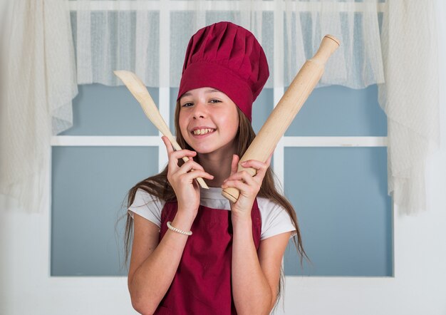 Servizio di pulizie e aiuto domestico. sviluppo dell'infanzia. piccola ragazza che cuoce in cucina. chef bambino che cucina con mattarello e cucchiaio di legno. il bambino prepara cibo sano a casa e indossa l'uniforme da cuoco.