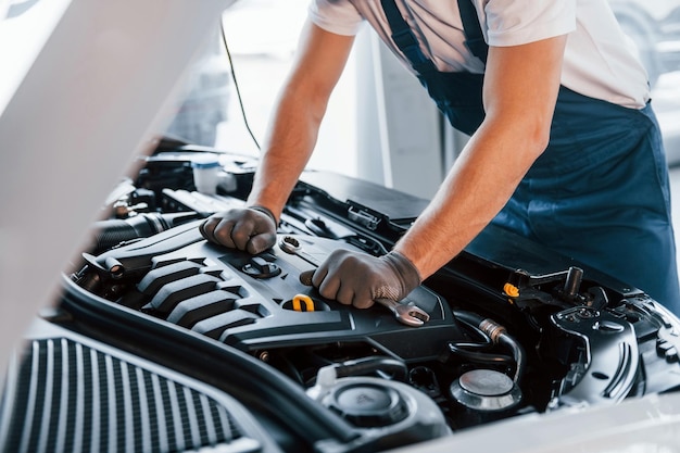 Servizio di qualità Il giovane in camicia bianca e uniforme blu ripara l'automobile