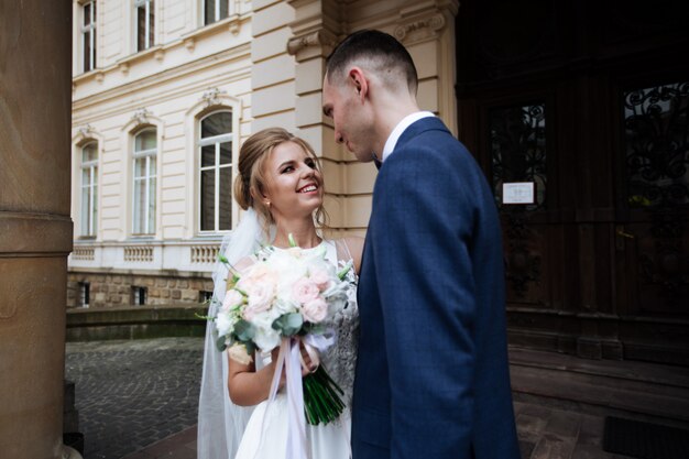 Servizio fotografico di matrimonio. Sposa e sposo che camminano nella città. Coppia sposata che si abbraccia e si guarda. Mazzo della holding. All'aperto, corpo pieno