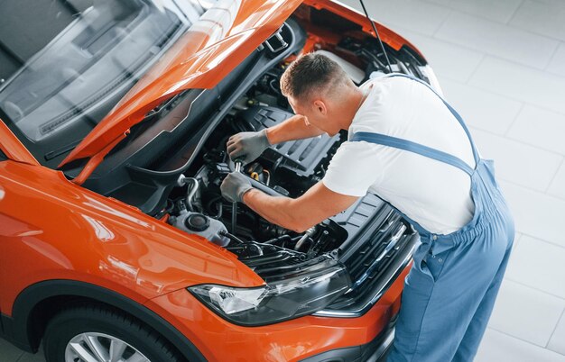 Servizio professionale L'uomo in uniforme sta riparando l'automobile rotta all'interno