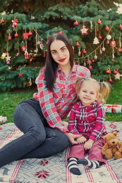 Sessione di foto del nuovo anno della famiglia della madre e della figlia a luglio vicino all'albero di Natale con i regali nel parco