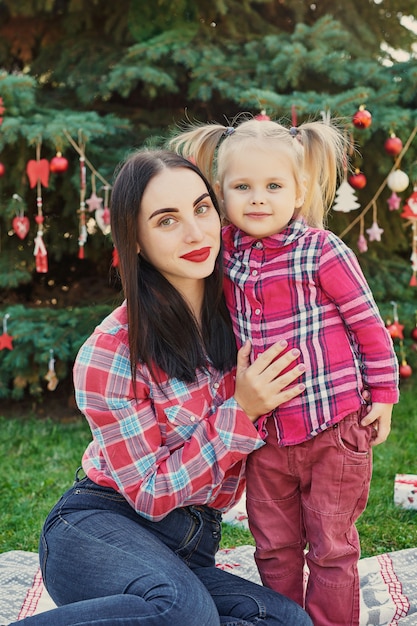 Sessione di foto del nuovo anno della famiglia della madre e della figlia a luglio vicino all'albero di Natale con i regali nel parco