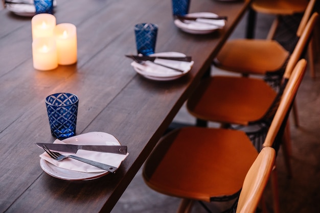 Set da pranzo composto da piatto bianco, posate e vetro blu sul tavolo di legno.