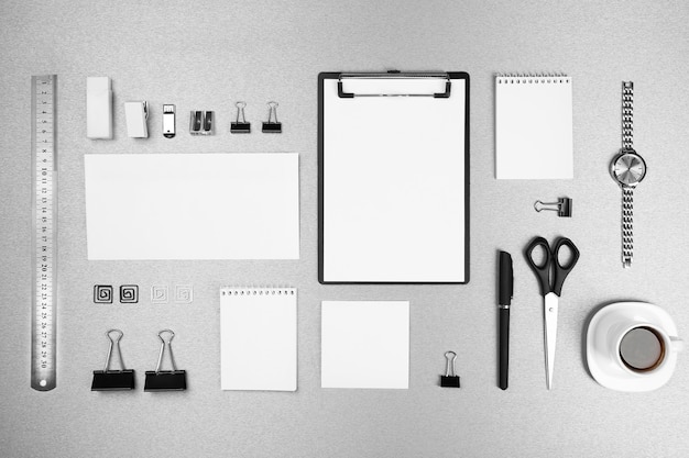Set da ufficio con fogli di carta bianchi, tazza di caffè, orologio e cancelleria su sfondo grigio