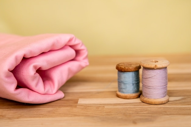 Set di accessori sartoriali. Primo piano di una pila di tessuto rosa piegato, forbici da cucito e bobine di filo