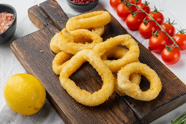 Set di anelli di calamari impanati al forno, su tavola da portata, su sfondo di tavolo in pietra bianca