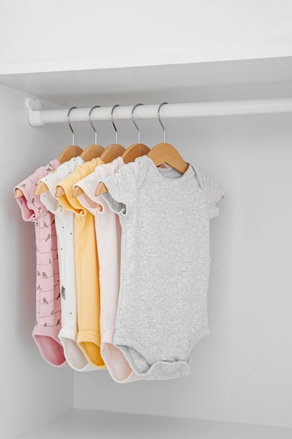 Set di body per neonato per bambina e bambino appesi su grucce nell'armadio bianco. Maternità, pulizia del guardaroba dei bambini a casa. Concetto di moda minimale.
