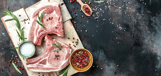 Set di braciole di carne di maiale biologica con spezie e rosmarino e pepe rosso su tavola nera Vista dall'alto in formato banner lungo
