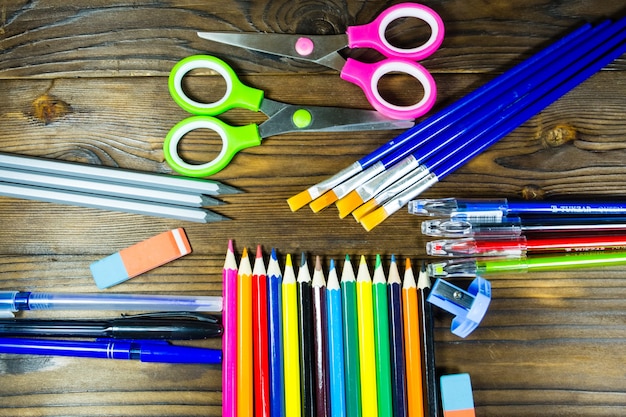 Set di cancelleria per la scuola. Matite colorate, penne, forbici, gomma, pennelli sulla scrivania in legno. Ritorno al concetto di scuola