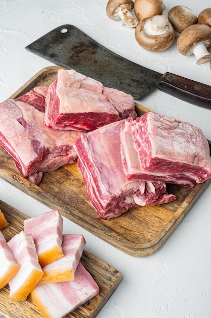 Set di carne a costine di vitello crudo di vitello, con ingredienti e vecchio coltello da macellaio, su fondo di pietra bianca