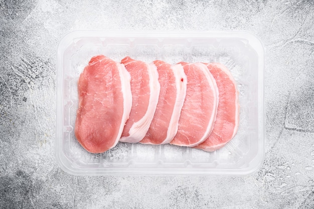 Set di carne di maiale fresca, in contenitore di plastica, su sfondo di tavolo in pietra grigia, vista dall'alto piatta